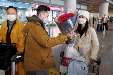 رجل يسلم الزهور لامرأة بعد وصولها مطار العاصمة بكين بعد أن رفعت الصين متطلبات الحجر الصحي (رويترز)